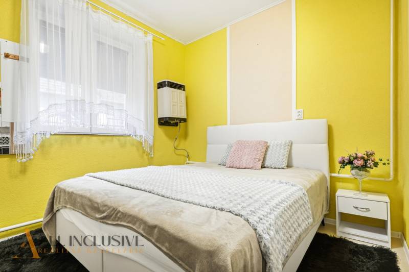 Bedroom in a family house with yellow walls, a white bed, and floral decoration.