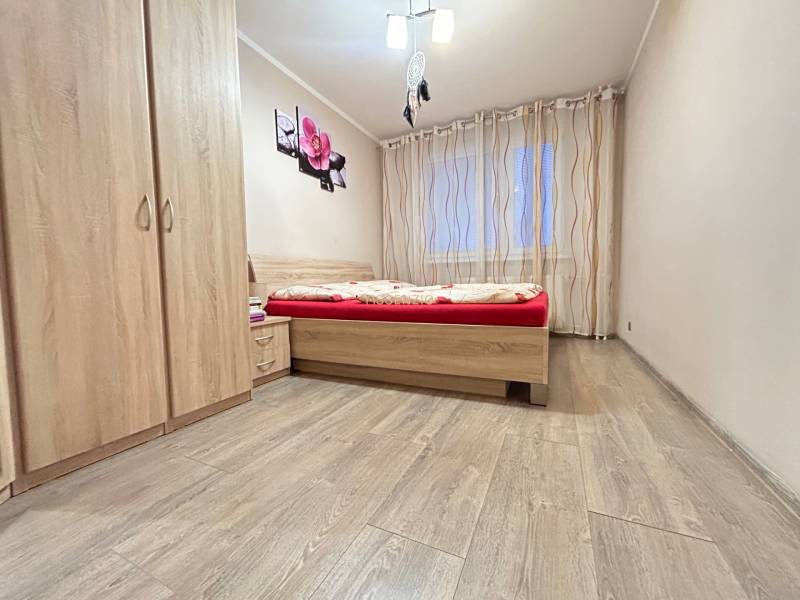Bedroom in a 2-room apartment with wood-patterned flooring, a bed, and a wardrobe.
