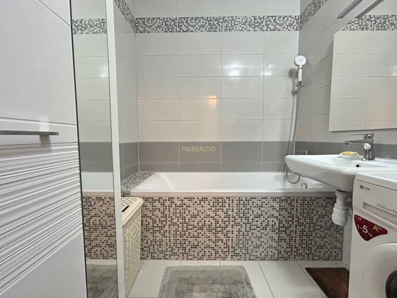 A bathroom in a 2-room apartment with a bathtub, washing machine, and mosaic tiles.