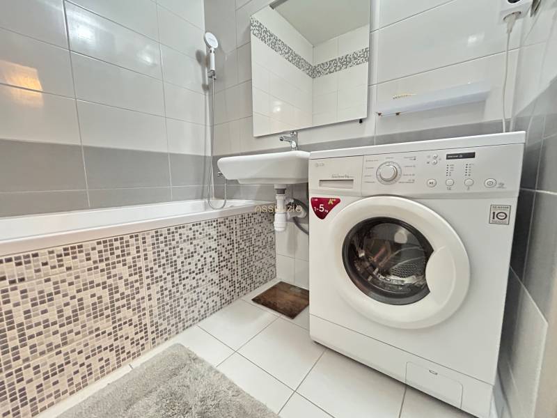 Bathroom with a bathtub and a washing machine in a 2-room apartment, tiles and white tiles.