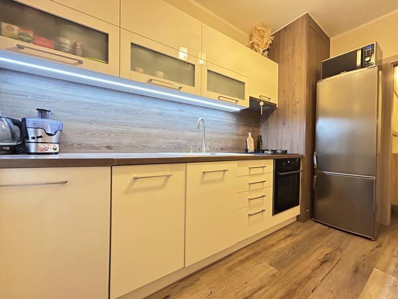 A kitchen in a 2-room apartment with a wooden decor floor, built-in appliances, and storage cabinets.