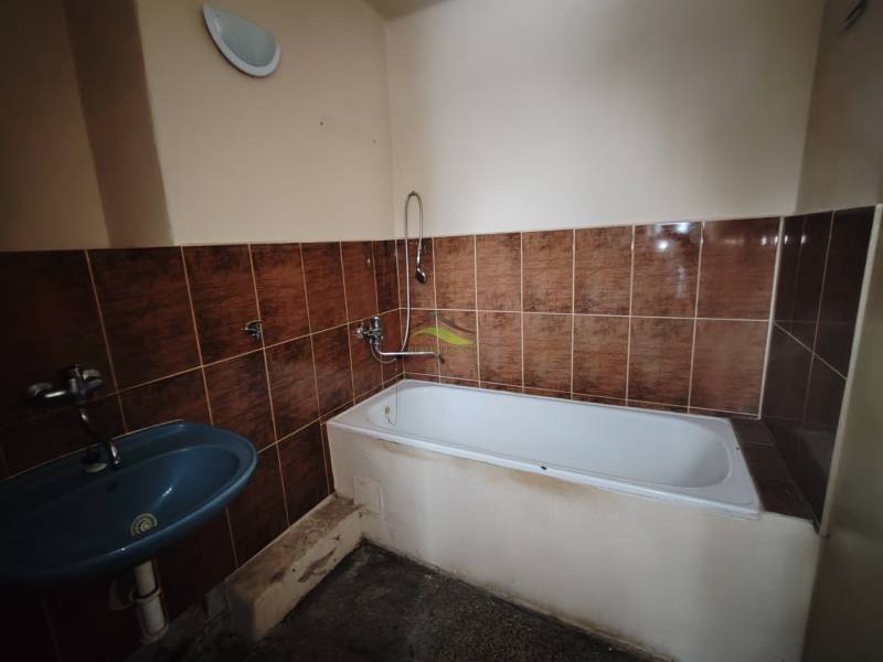 A bathroom with brown tiles, a bathtub, and a blue sink in a 2-room apartment.
