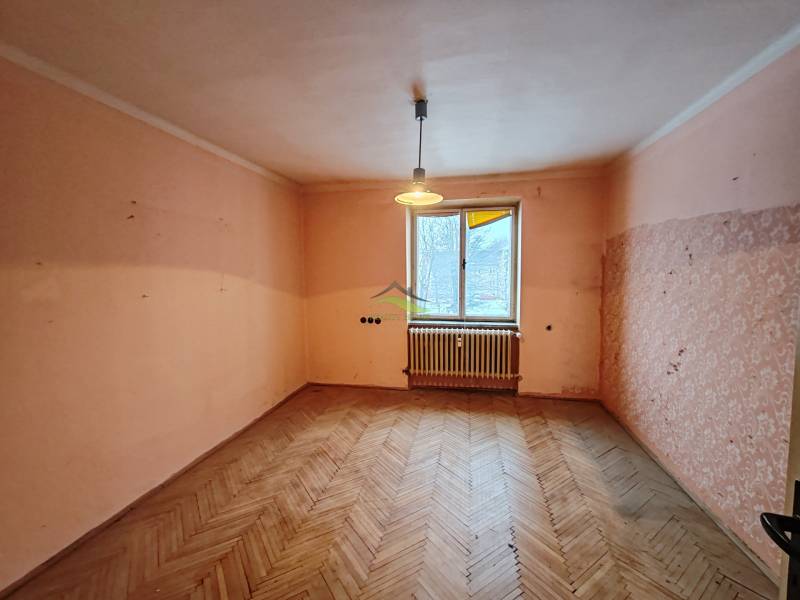 A room in a 2-room apartment with a wooden decor floor and a window with a radiator.