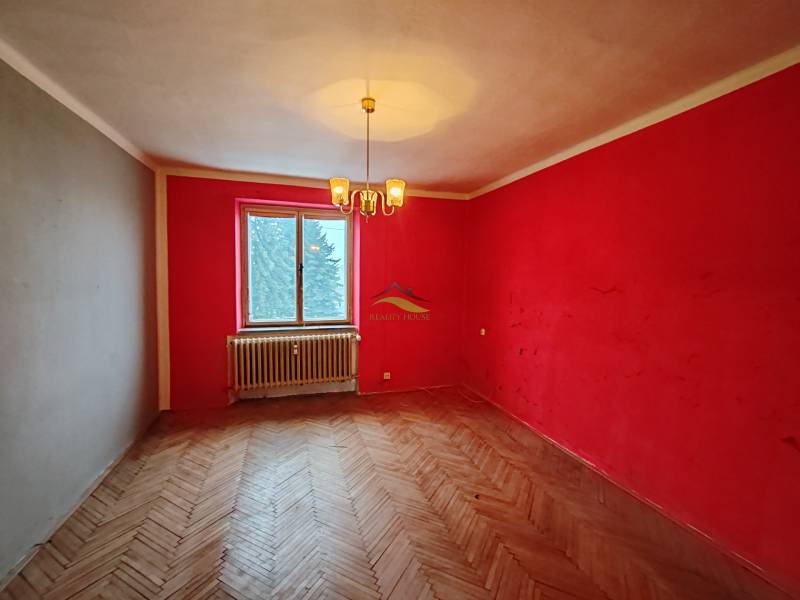 A room with red walls, a chandelier, and a wooden decor floor in a two-room apartment.