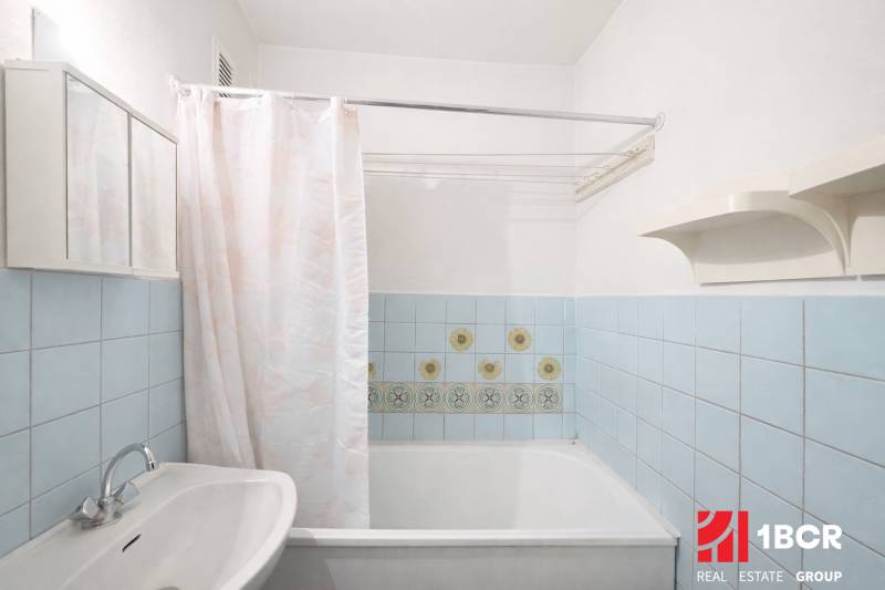 A bathroom in a studio apartment with a bathtub, a sink, and light blue tiles.