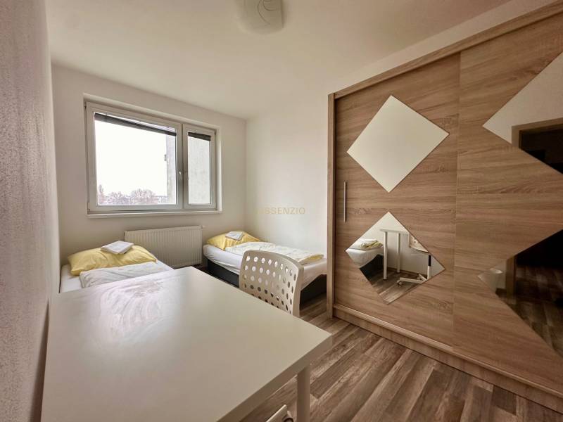 A bedroom with two beds, a white table, and a wardrobe in a three-room apartment.