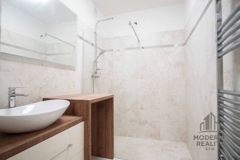 A bathroom in a family house with a sink and a shower, wood decor and light tiles.