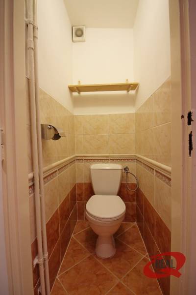 A toilet with tiles in a 3-room apartment with a practical shelf.