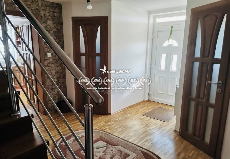 A hallway of a family house with a wooden decor floor and a staircase with a metal railing.