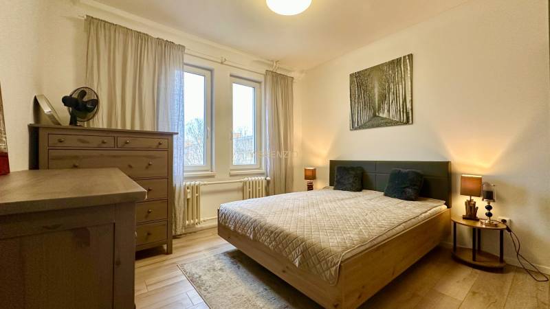 Bedroom in a 2-room apartment with a double bed, dresser, and wooden decor flooring.