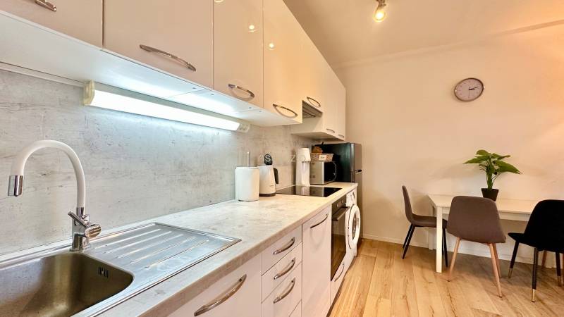 A kitchen in a 2-room apartment with a wooden decor floor, a dining table, and appliances.