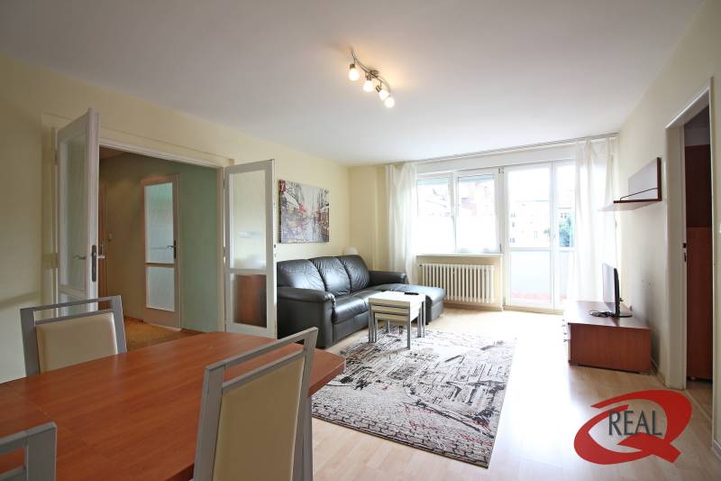 Living room in a three-room apartment with a wooden decor floor and a black sofa.