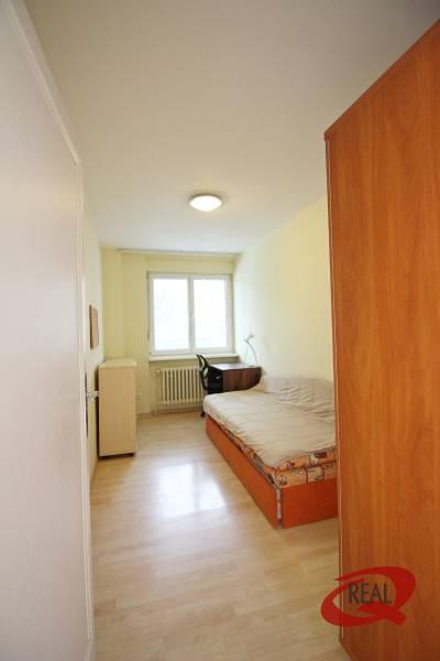 A narrow room with a bed, a table, and a wardrobe, a floor with a wooden decor in a 3-room apartment.