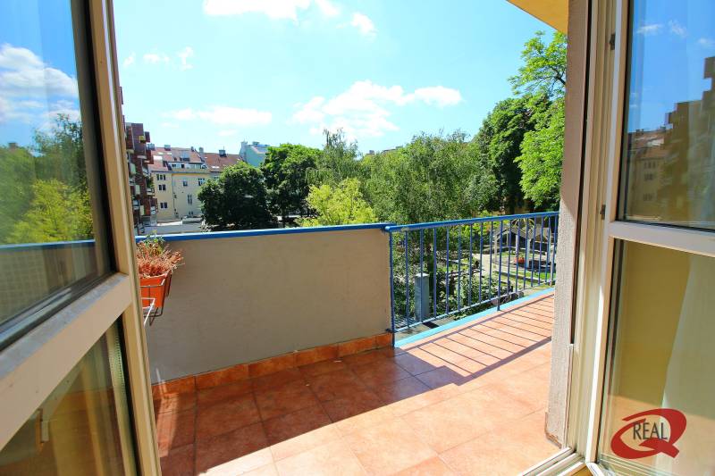 A balcony of a 3-room apartment with a view of greenery and other buildings.