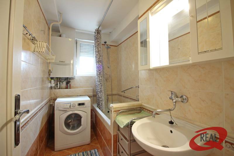 A bathroom with a bathtub and a washing machine in a 3-room apartment, with cream-colored tiles.