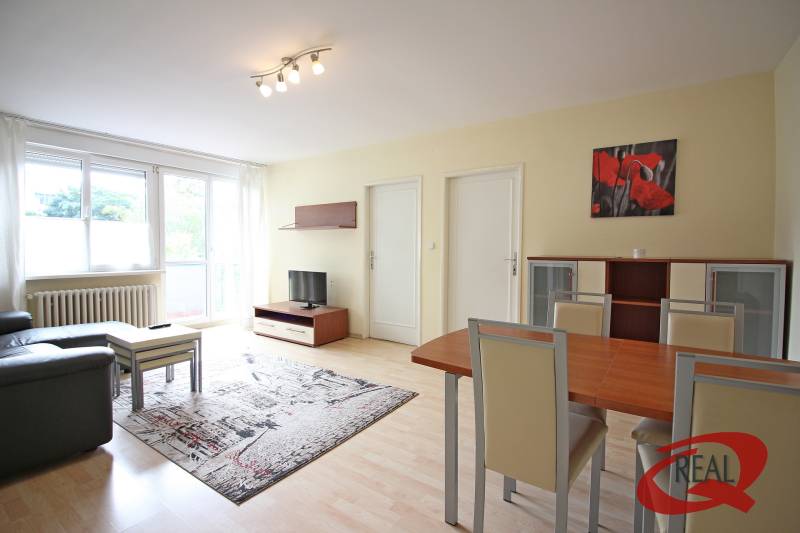 Living room in a three-room apartment with a wooden decor floor, a sofa, and a dining table.