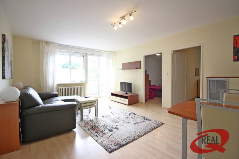 Living room of a three-room apartment with a sofa, table, and television on a wooden-decor floor.