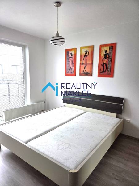 A bedroom with a double bed, a lamp, and paintings in a studio apartment.