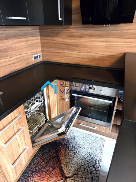 A kitchen in a studio apartment with a built-in dishwasher and wooden decor.