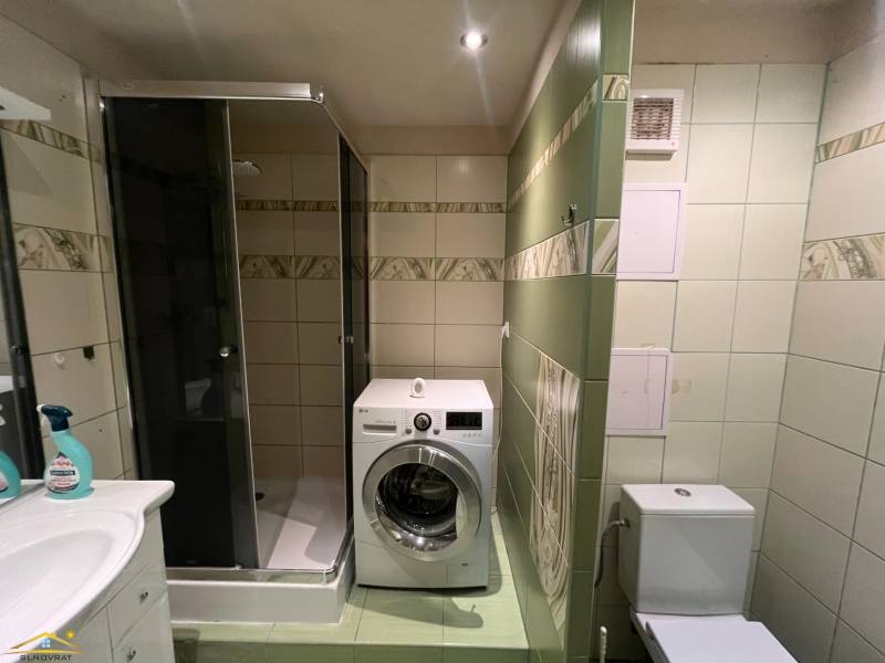Bathroom in a 2-room apartment with a washing machine, shower, and toilet.