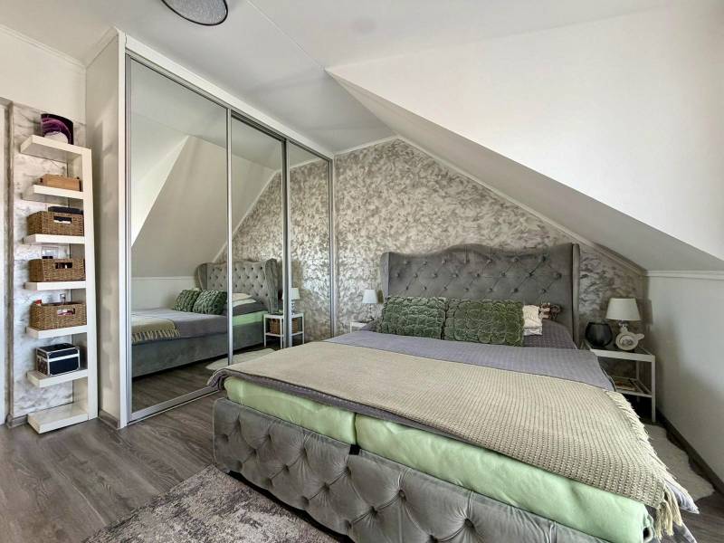Interior of a 2-room apartment with a wooden decor floor, slanted ceiling, and mirrored wardrobe.