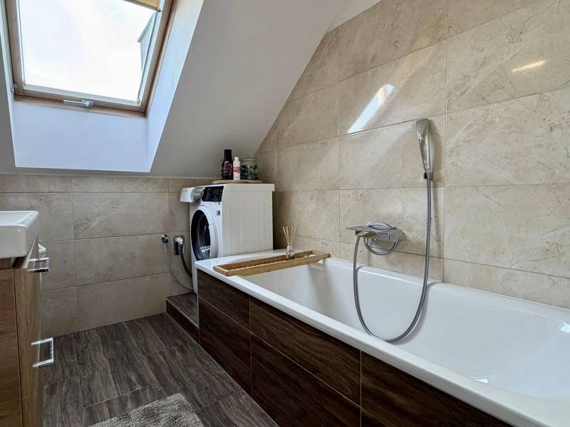 A bathroom with a skylight, a washing machine, and a wooden decor floor in a 2-room apartment.