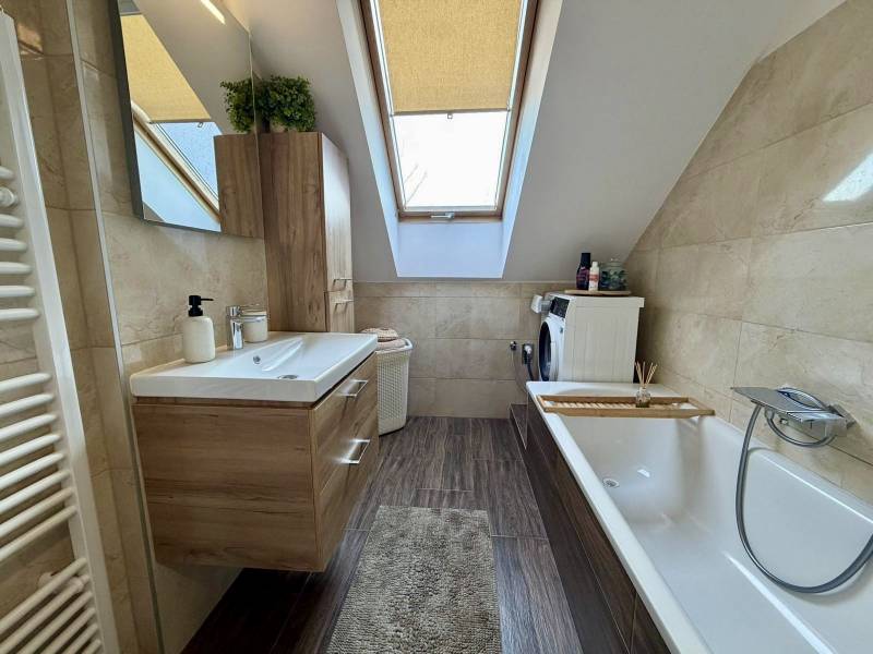 A bathroom in a two-room apartment with a wooden decor floor, a bathtub, and a skylight.