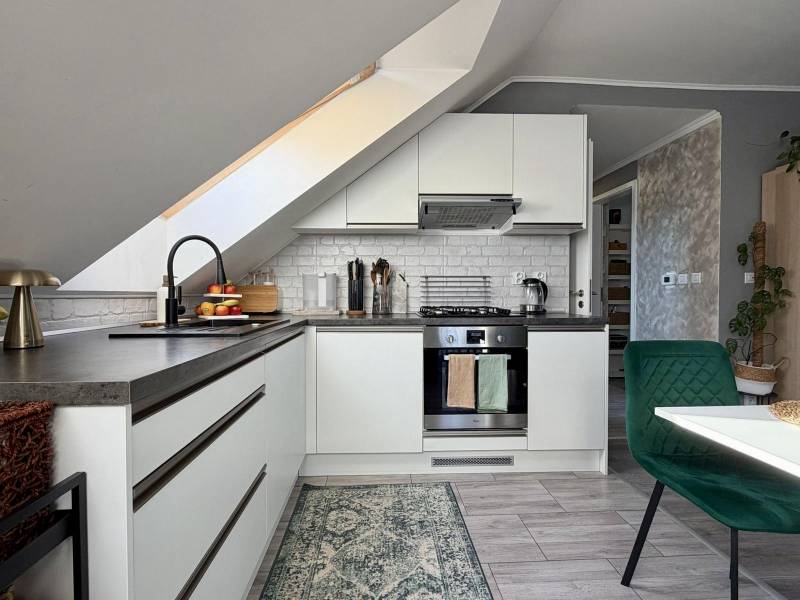 A kitchen in a 2-room apartment with a slanted ceiling and a floor with a wooden decor.
