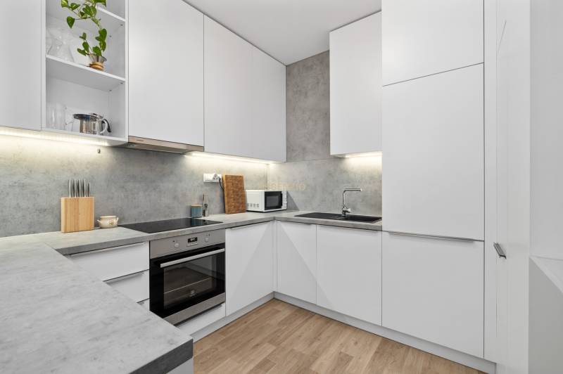 A kitchen in a 3-room apartment with white cabinets and a wooden decor floor.