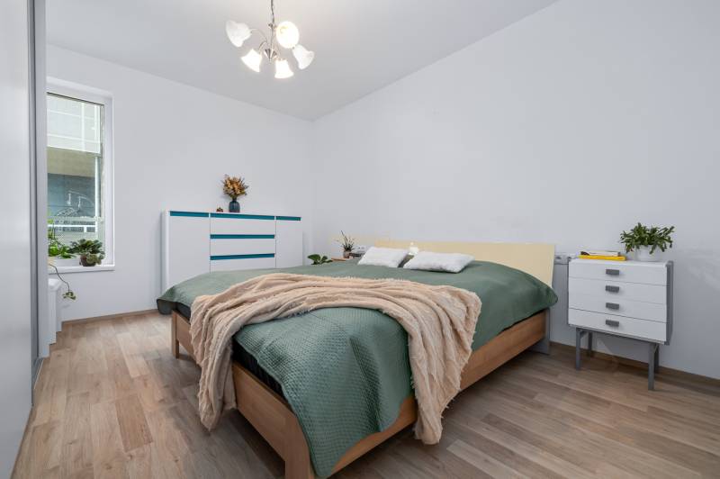 Bedroom with a bed, dresser, plants, and wood-decor flooring in a 3-room apartment.