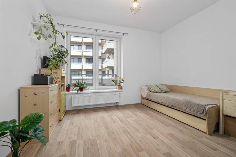 A room in a 3-room apartment with a wooden decor floor, a bed, and plants.