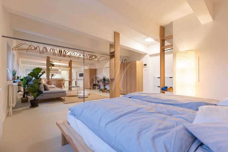 A bright bedroom in a 3-room apartment with a bed, plants, and an open space.