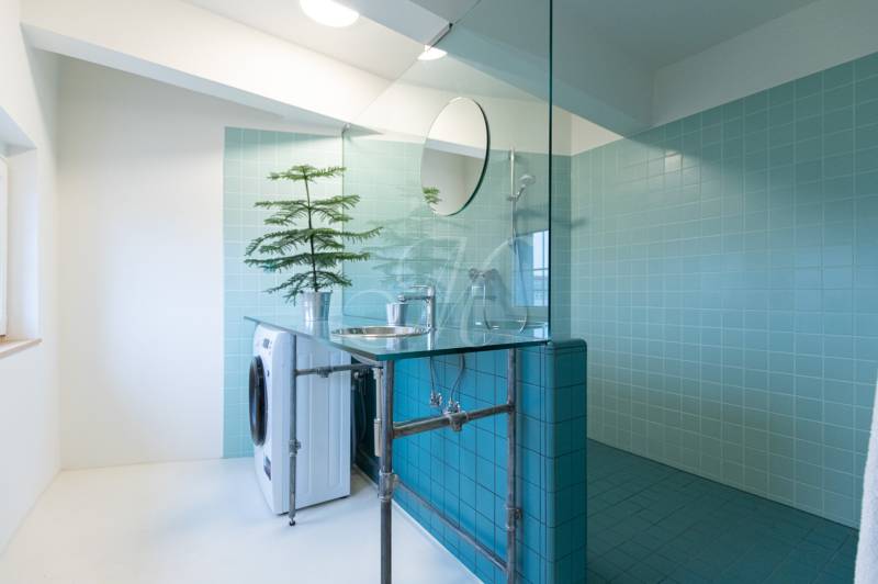 A bathroom with blue tiles, a shower, a washing machine, and a sink in a 3-room apartment.