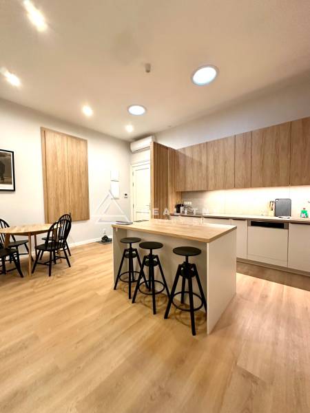 A kitchen in a 2-room apartment with an island, chairs, and a wooden decor floor.