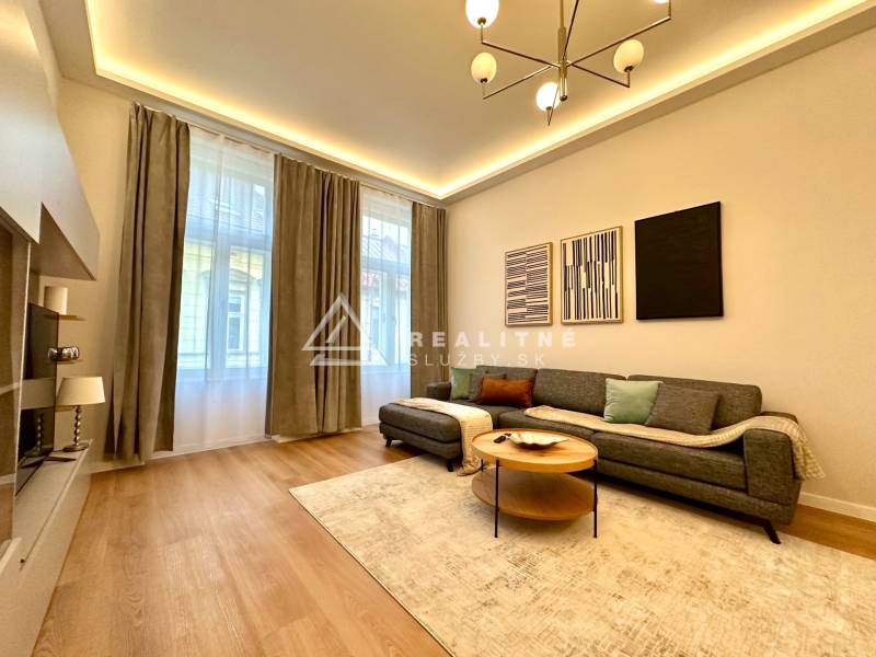 Living room in a two-room apartment with a wooden decor floor, gray sofa, and decorative paintings.