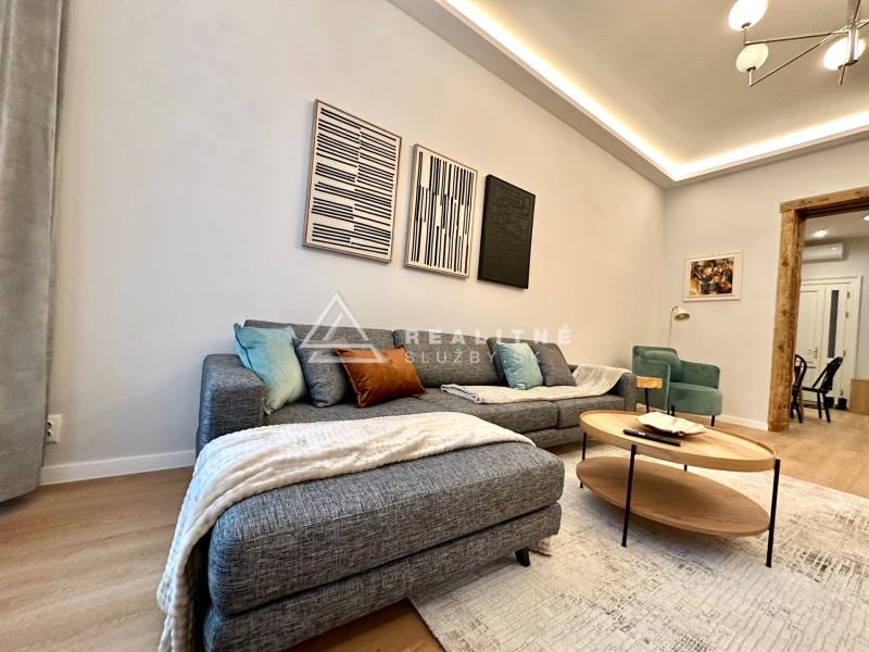 Living room with a sofa, wood-patterned flooring, and artworks in a 2-room apartment.