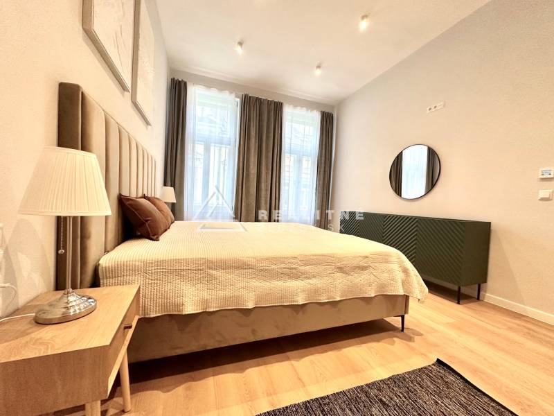 Bedroom in a 2-room apartment with a large bed, lamp, and floor with wood decor.