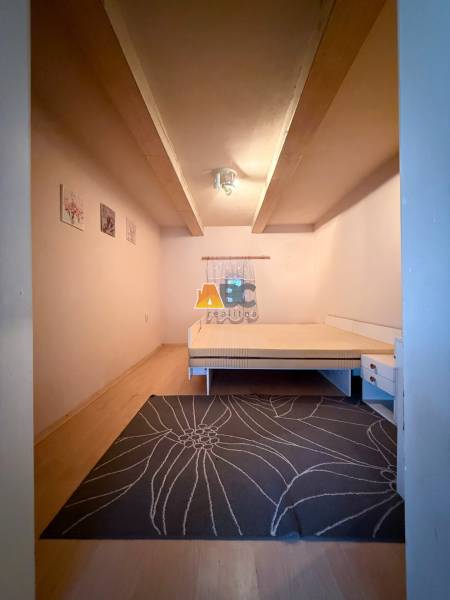 A simply furnished room in a cottage with carpet and wood-patterned flooring.