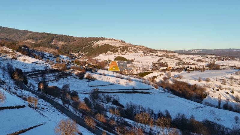 A snowy landscape with a cottage on Zánemecká Street in Hriňová, surrounded by hills.