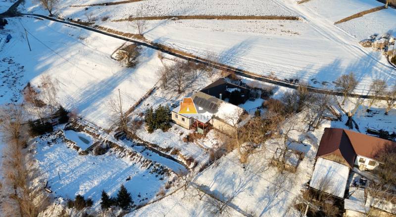 A snowy landscape with a cottage on Zánemecká Street in Hriňová, surrounded by fields and roads.