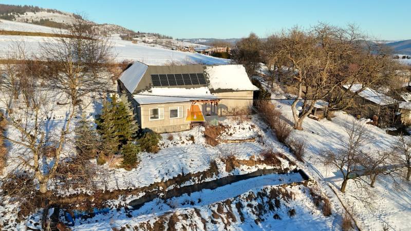 A cottage on Zánemecká Street in Hriňová, surrounded by a snowy hilly landscape with solar panels.