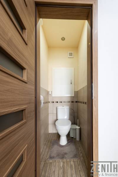 A toilet with ceramic tiles and a wooden decor floor in a 3-room apartment.
