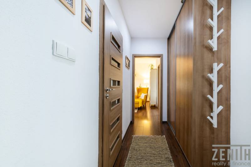 A hallway of a 3-room apartment with a wooden decor floor, wooden doors, and a yellow armchair.