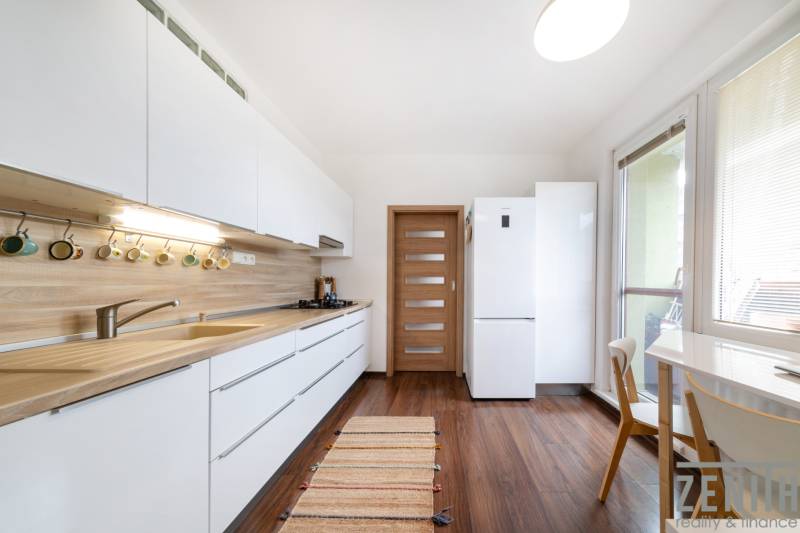 A bright kitchen in a 3-room apartment with white cabinets and a wood-patterned floor.