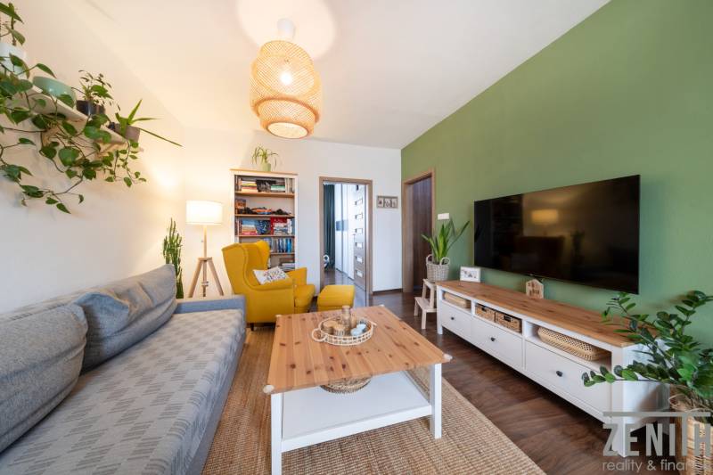 Living room in a 3-room apartment with a television, wooden decor flooring, and a comfortable armchair.