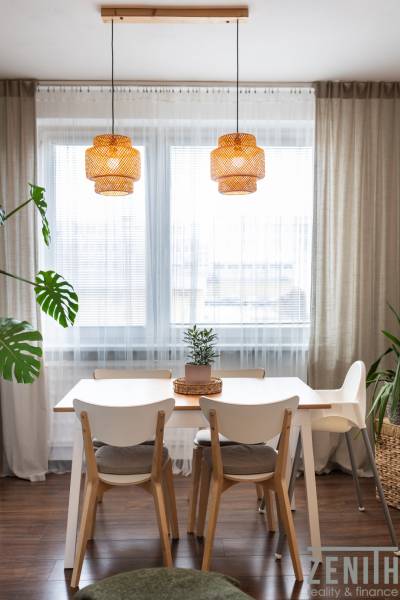 Dining area with a table, chairs, and a plant in a 3-room apartment with wooden decor flooring.