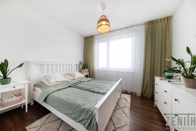 A bright bedroom with white furniture, wood-patterned flooring, and plants in a 3-room apartment.