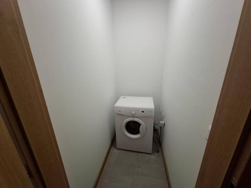 A washing machine in a narrow room with a wooden decor floor in a 5 or more room apartment.