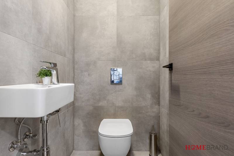 Compact toilet in a 3-room apartment with modern gray tiles and a small sink.