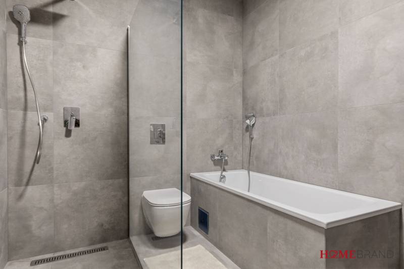 A bathroom with a bathtub and shower in a 3-room apartment, tiled with gray tiles.